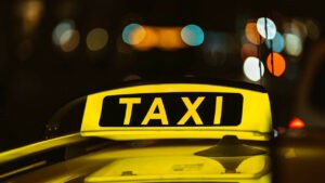 Black and yellow sign of Taxi at night placed on top of a car